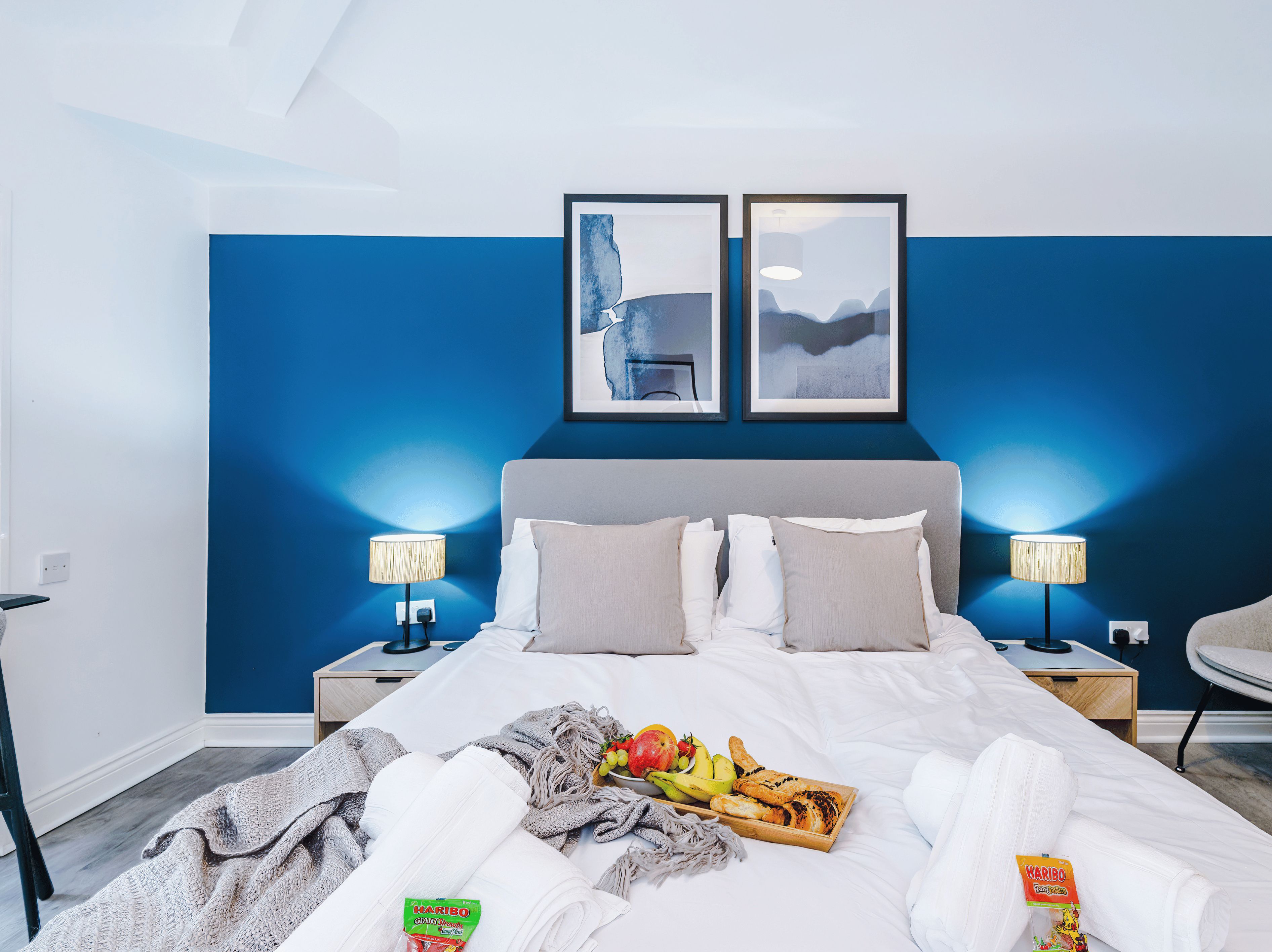 A hotel room with a bed, two bedside tables, a chair, and artwork on the wall.