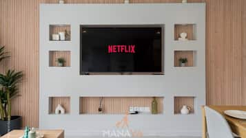 Un salon moderne avec un téléviseur fixé au mur qui affiche le mot « NETFLIX » en lettres rouges, entouré d’étagères en bois ornées d’objets décoratifs et de plantes.