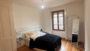 Un dormitorio con una cama, suelo de madera, una ventana y un armario blanco.