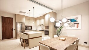 Een moderne keuken met een centraal eiland, barkrukken en een eettafel met stoelen.