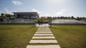 Een pad dat leidt naar een modern gebouw met een glazen gevel, omringd door een gazon en een waterpartij.