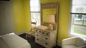 A room with a bed, a dresser with drawers, a chair, and a window with blinds. - Fountain Point - Hotel Room 1 (Lake Leelanau)