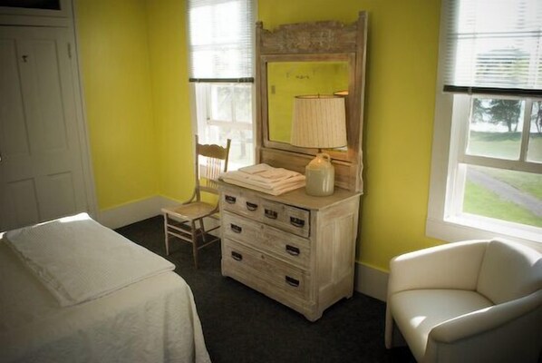 A room with a bed, a dresser with drawers, a chair, and a window with blinds.