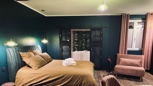 A bedroom with a bed, a chair, a table, and a door with a window. - Romantic Suite "Love Room" with Jacuzzi (Sainte-Eusoye)