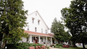 A large white building with a red roof, surrounded by lush greenery and outdoor seating.