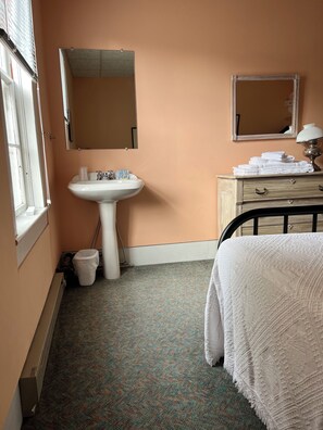 A bathroom with a sink, mirror, and a bed with a white blanket.