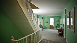 Un couloir aux murs verts, avec un escalier en bois et un sol recouvert de moquette.