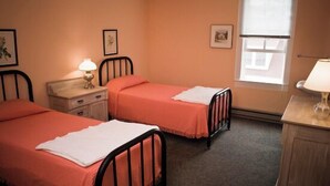 A bedroom with two single beds, a nightstand with a lamp, a dresser, and a window with blinds. - Fountain Point - Hotel Room 6 (Lake Leelanau)