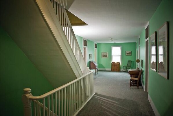 A hallway with green walls, a wooden staircase, and a carpeted floor.