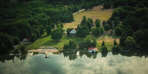 An aerial view of a lakeside property with a dock, a small house with a red roof, and a grassy area.