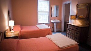 Een hotelkamer met twee bedden, een nachtkastje met een lamp, een dressoir, een raam en een wastafel.