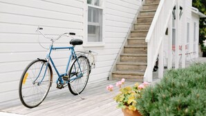 A blue bicycle parked on a wooden deck in front of a white house with a staircase. - Fountain Point - Hotel Room 14 (Lake Leelanau)