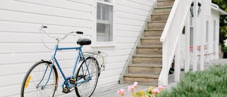 A blue bicycle parked on a wooden deck in front of a white house with a staircase.