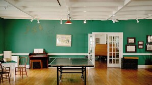 A room with a ping pong table, a piano, chairs, and a green wall with framed pictures. - Fountain Point - Hotel Room 14 (Lake Leelanau)