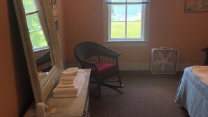 A bedroom with a large mirror, a rocking chair, a bed, and a window with blinds. - Fountain Point - Hotel Room 15 (Lake Leelanau)