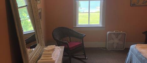 Ein Schlafzimmer mit großem Spiegel, Schaukelstuhl, Bett und Fenster mit Jalousien.