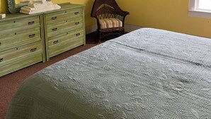 A bedroom with a bed, a dresser, a chair, a mirror, and a picture on the wall. - Fountain Point - Hotel Room 17 (Lake Leelanau)