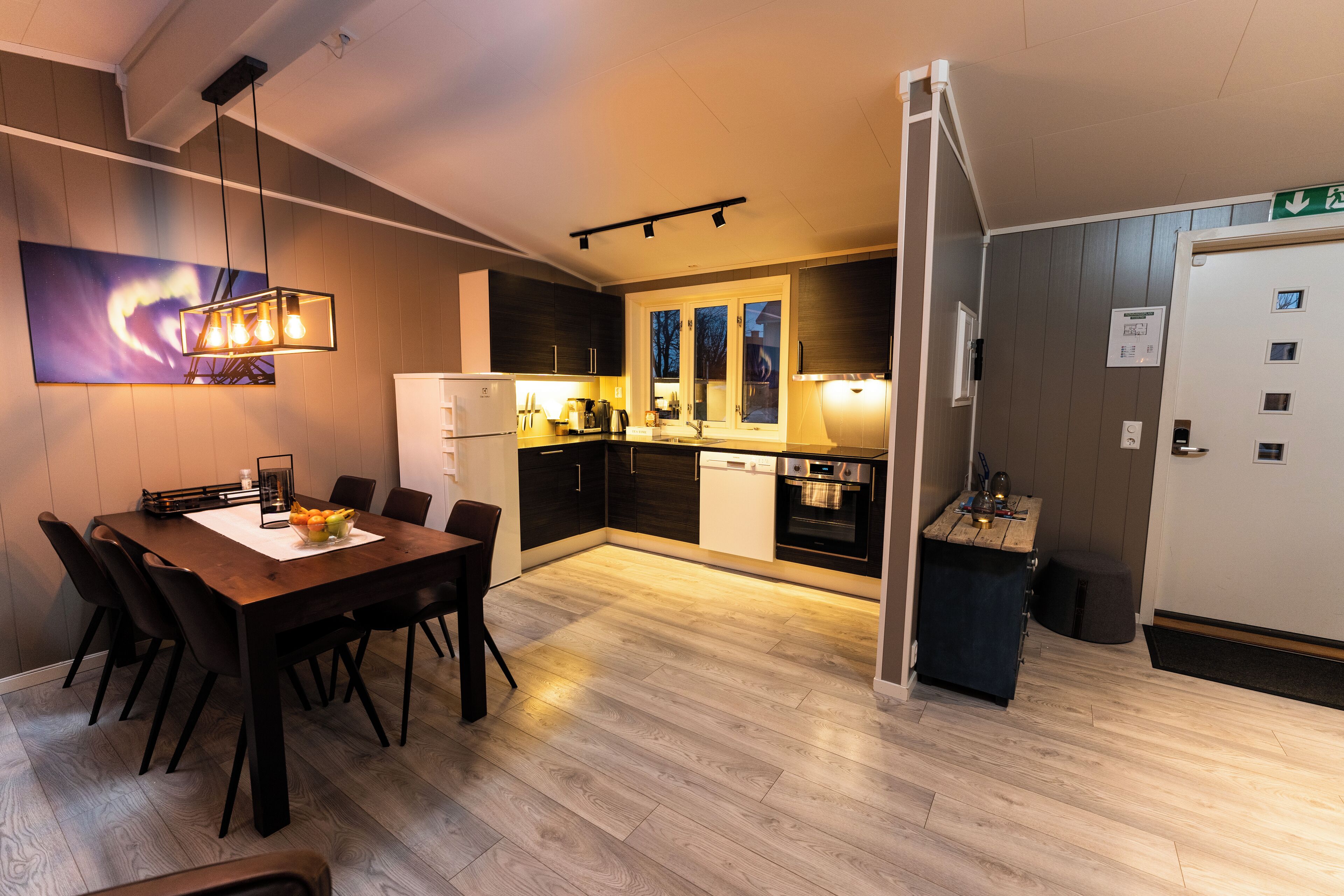 Una cocina moderna con comedor, suelo de madera e iluminación colgante.