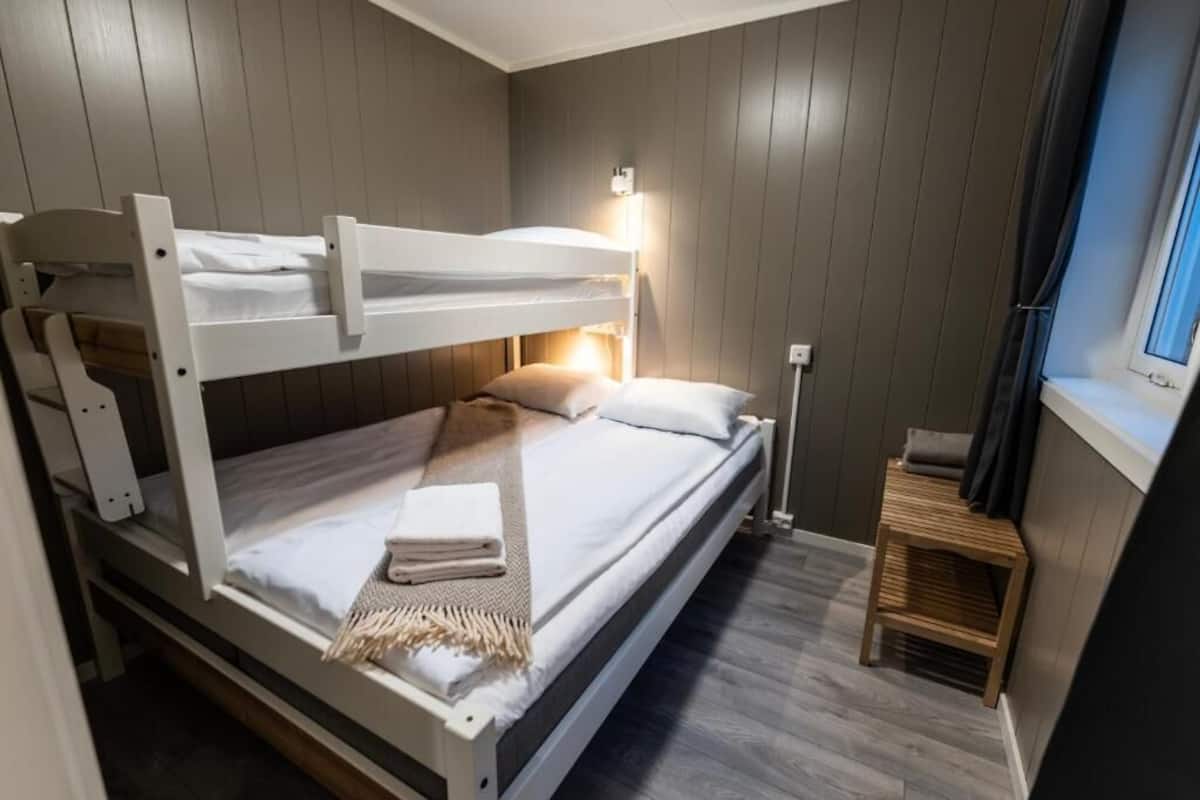 A bunk bed room with a small wooden stool and a nightstand.