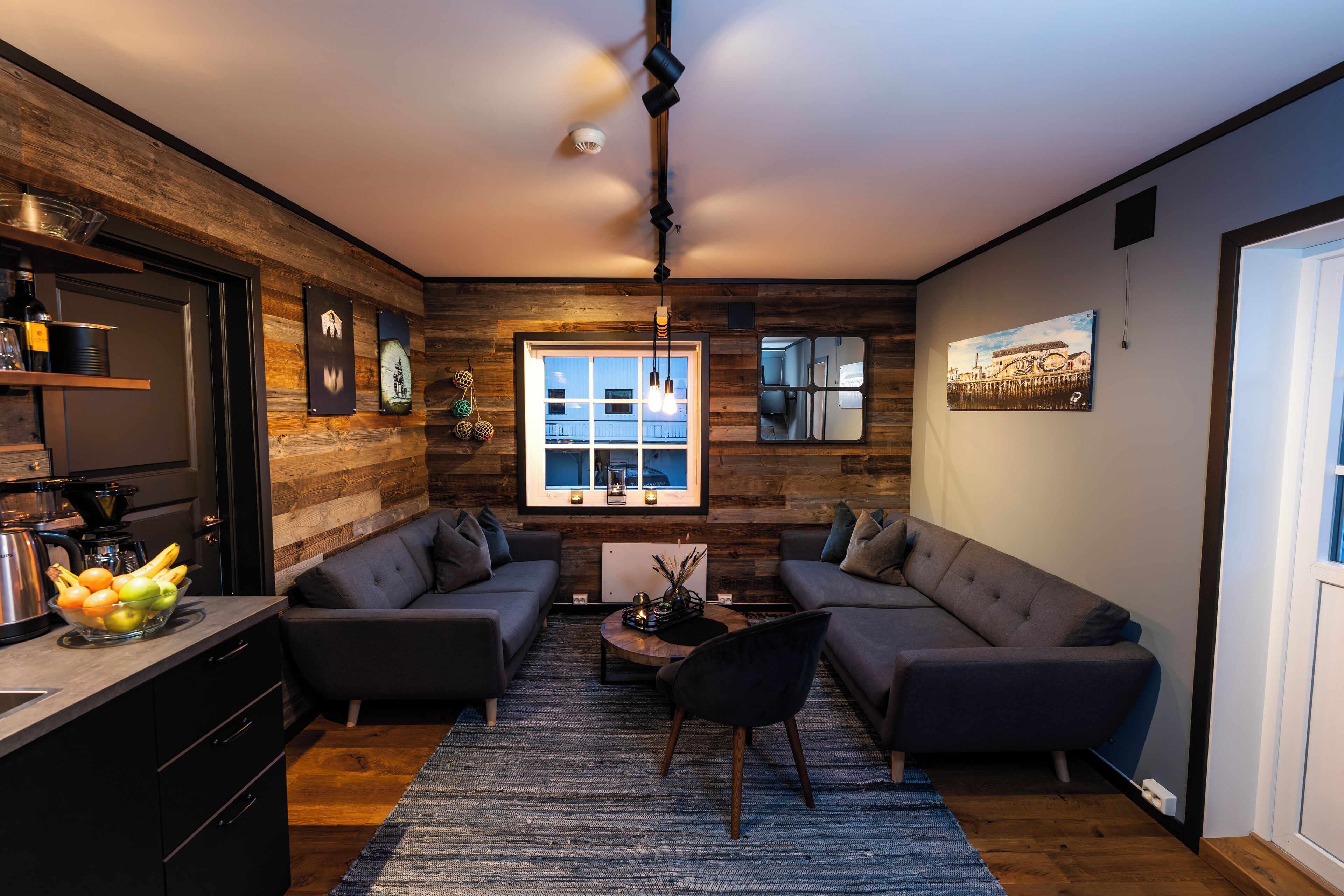 Un salon moderne avec un mur d’accent en bois, une grande fenêtre et un espace cuisine intégré.