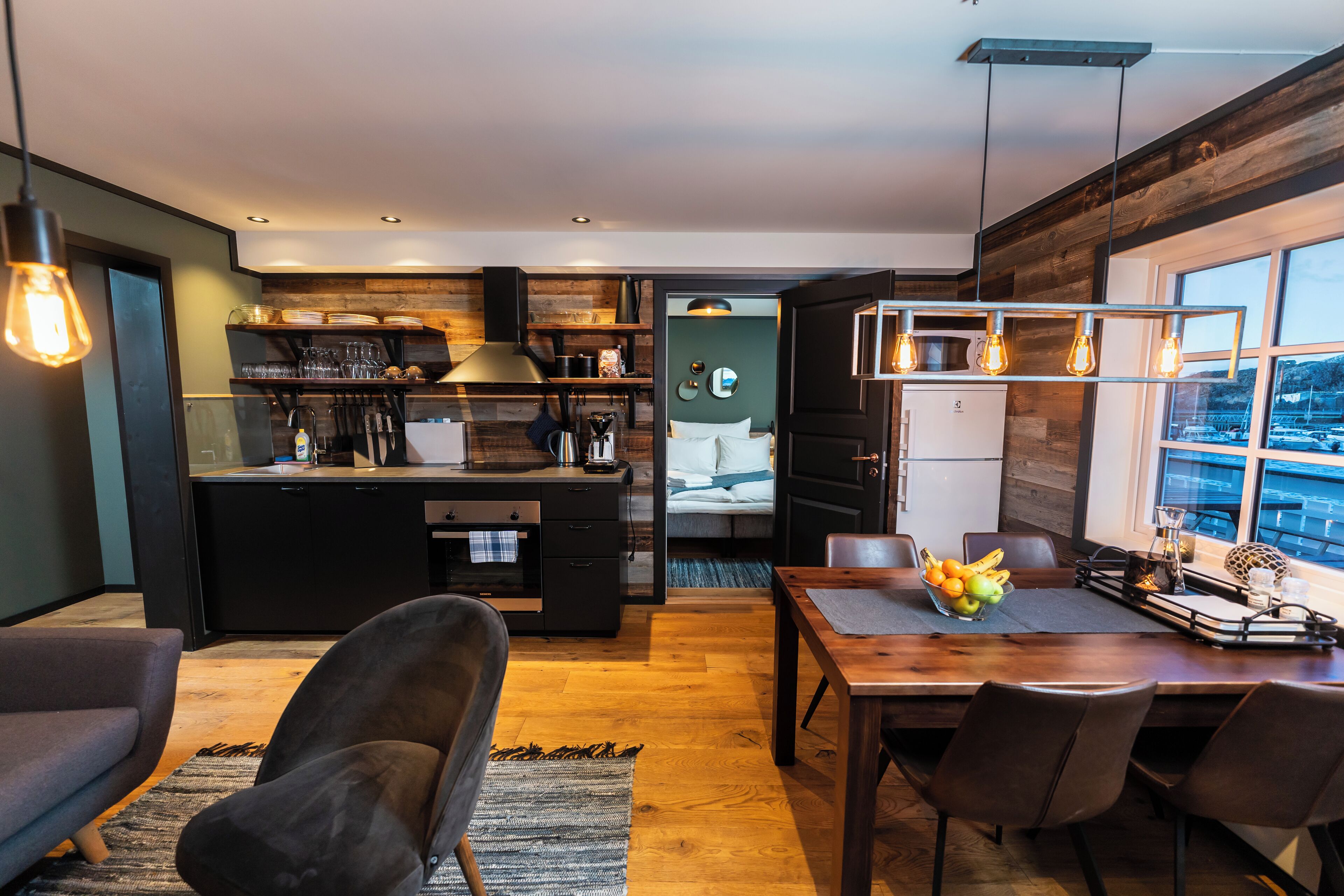 Una cocina moderna con detalles de madera, un comedor con fruteros y vistas a través de un ventanal.