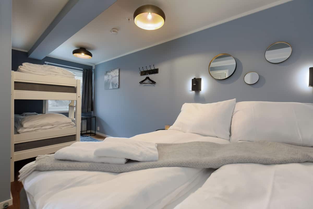 A bedroom with bunk beds, a bed with white linens, a grey throw blanket, and wall-mounted mirrors.