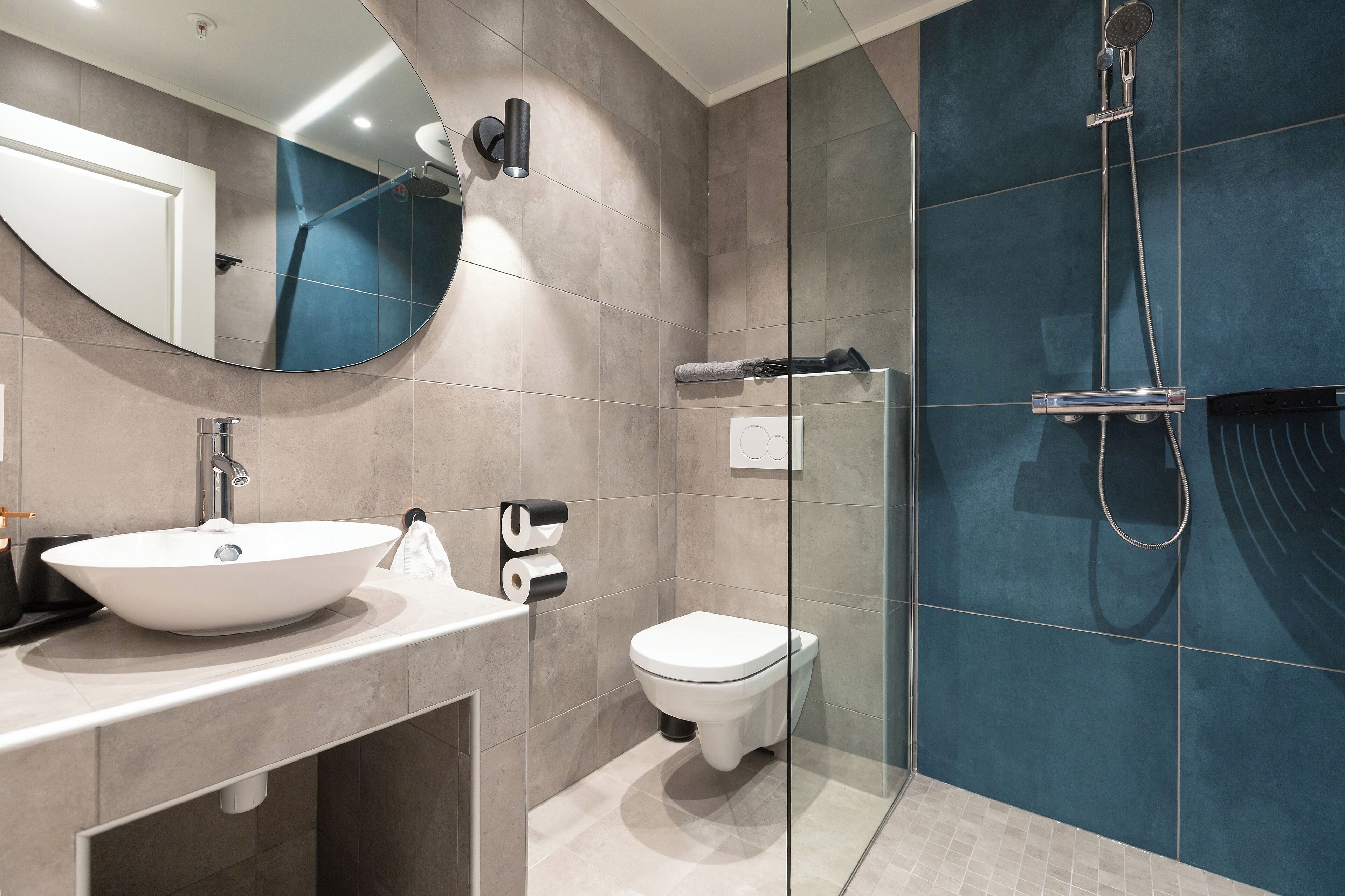 A modern bathroom with a large mirror, a white sink, a toilet, and a glass-enclosed shower area.