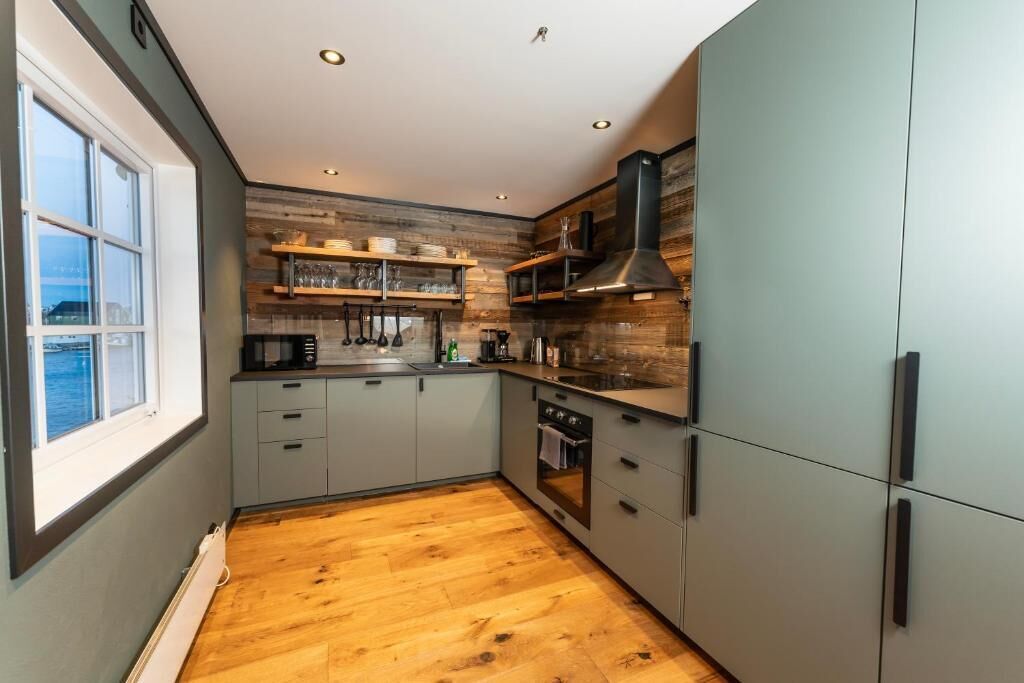 A modern kitchen with wooden flooring, grey cabinets, and a window overlooking a body of water.