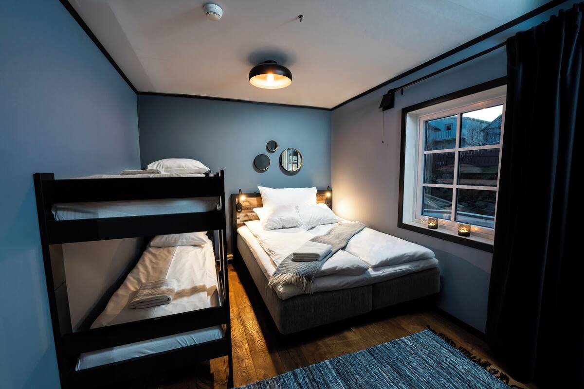 A bedroom with bunk beds, a window with curtains, and a wall-mounted light fixture.
