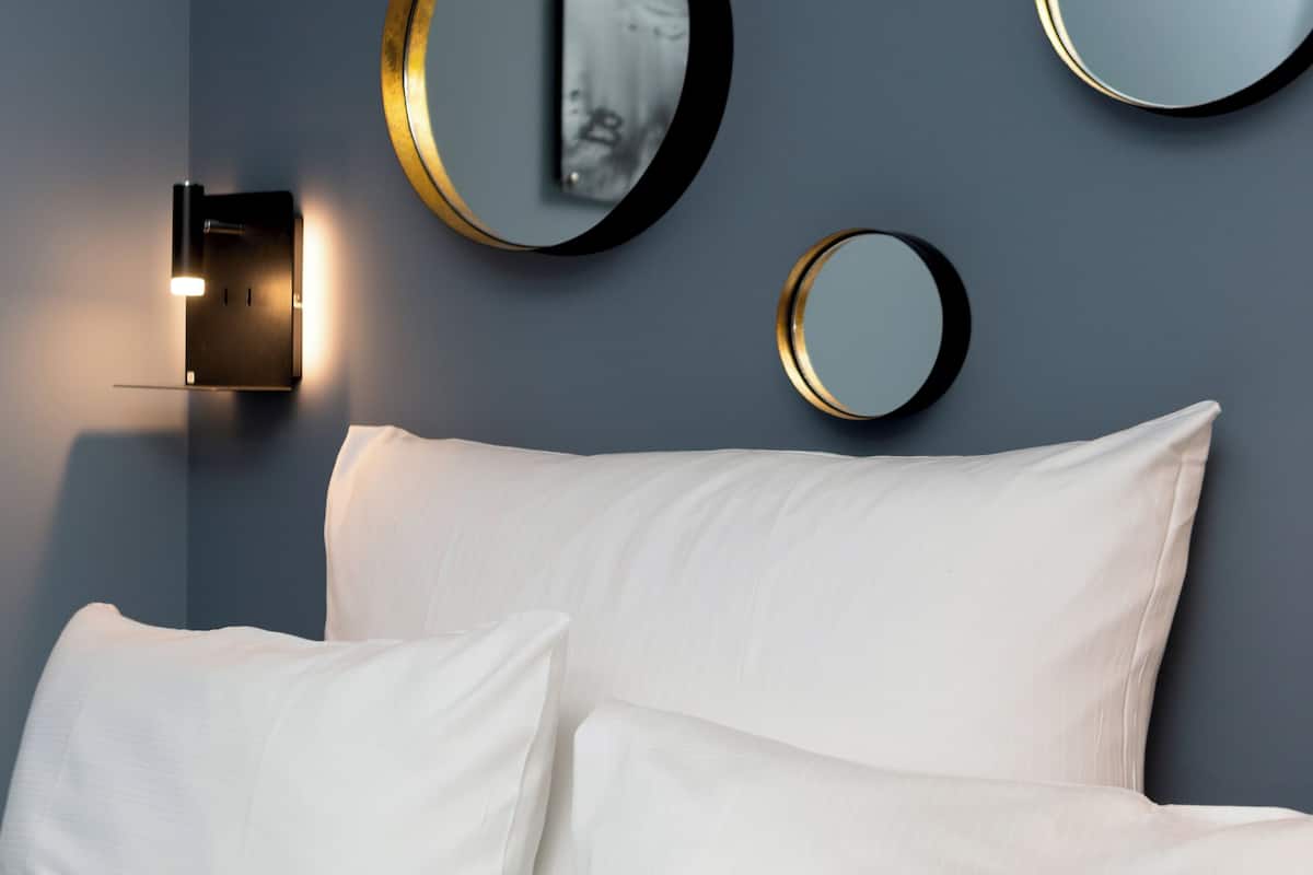 A bedroom with a bed, white bedding, and three wall-mounted mirrors.