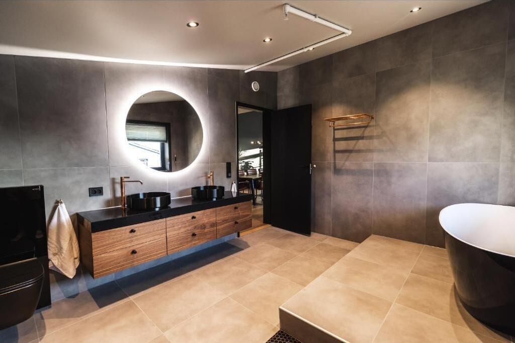 Un baño moderno con una bañera grande, un espejo redondo y un mueble de tocador oscuro.