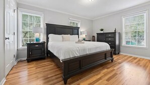 A bedroom with a dark wooden bed, white bedding, a nightstand with a lamp, and a dresser. - Gainesville Hideaway (Gainesville)
