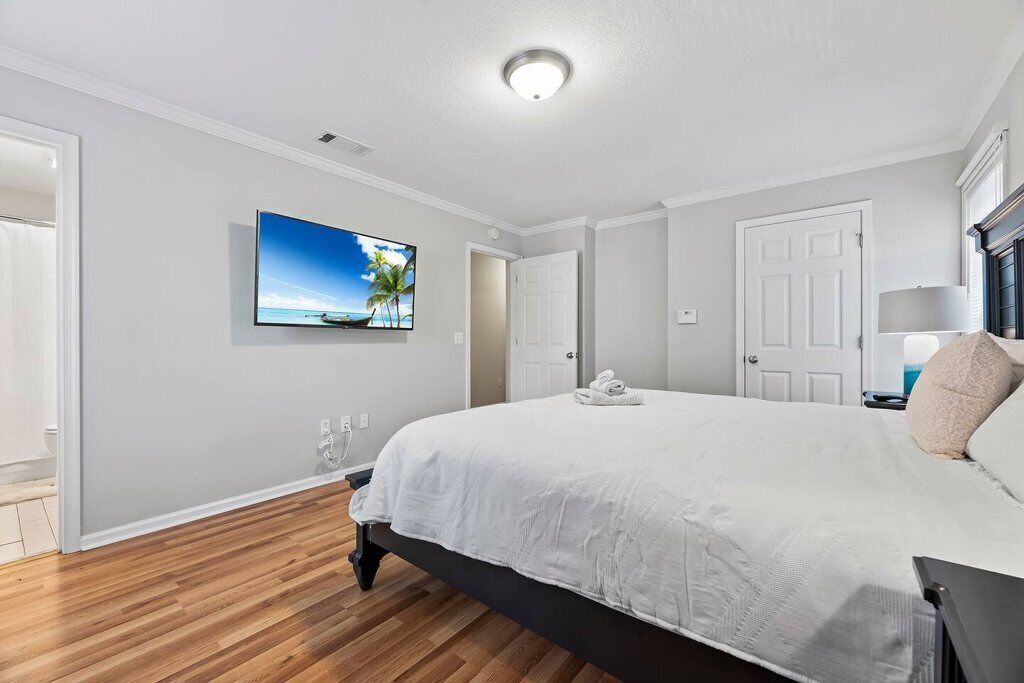 Une chambre dotée d’un grand lit, d’un téléviseur à écran plat fixé au mur et d’une porte donnant sur une autre pièce.