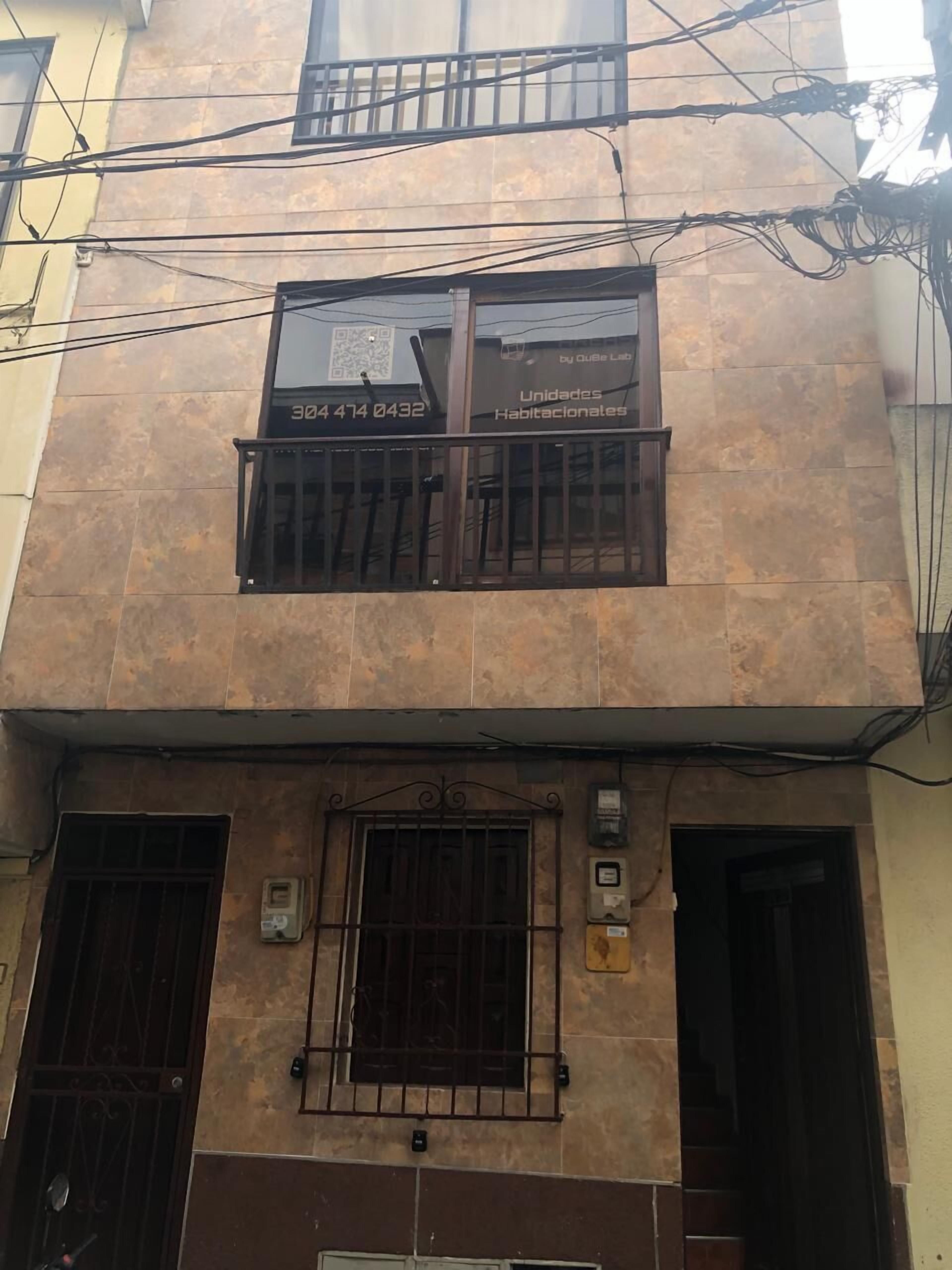 Un edificio con fachada de tejas, un balcón con barandilla metálica y una puerta con reja de metal.