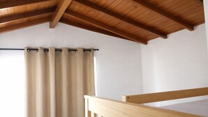 Una habitación con techo de madera, cortina color beige y baranda de madera.