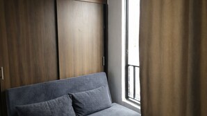 Una habitación con sofá, ventana con cortinas y armarios de madera.