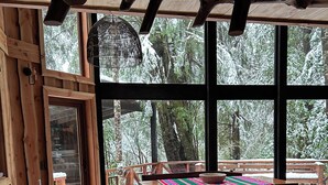 A wooden interior with large windows, a wooden table, benches, and a view of snow-covered trees. - House in Huilo Huilo, The Refuge of Fairies and Elves (Neltume)