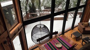 A cozy room with large windows, a hanging light fixture, a wooden table, and a view of a snowy deck outside. - House in Huilo Huilo, The Refuge of Fairies and Elves (Neltume)