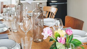 Et spisebord dækket med blanke glas, tallerkener og en vase med blomster.
