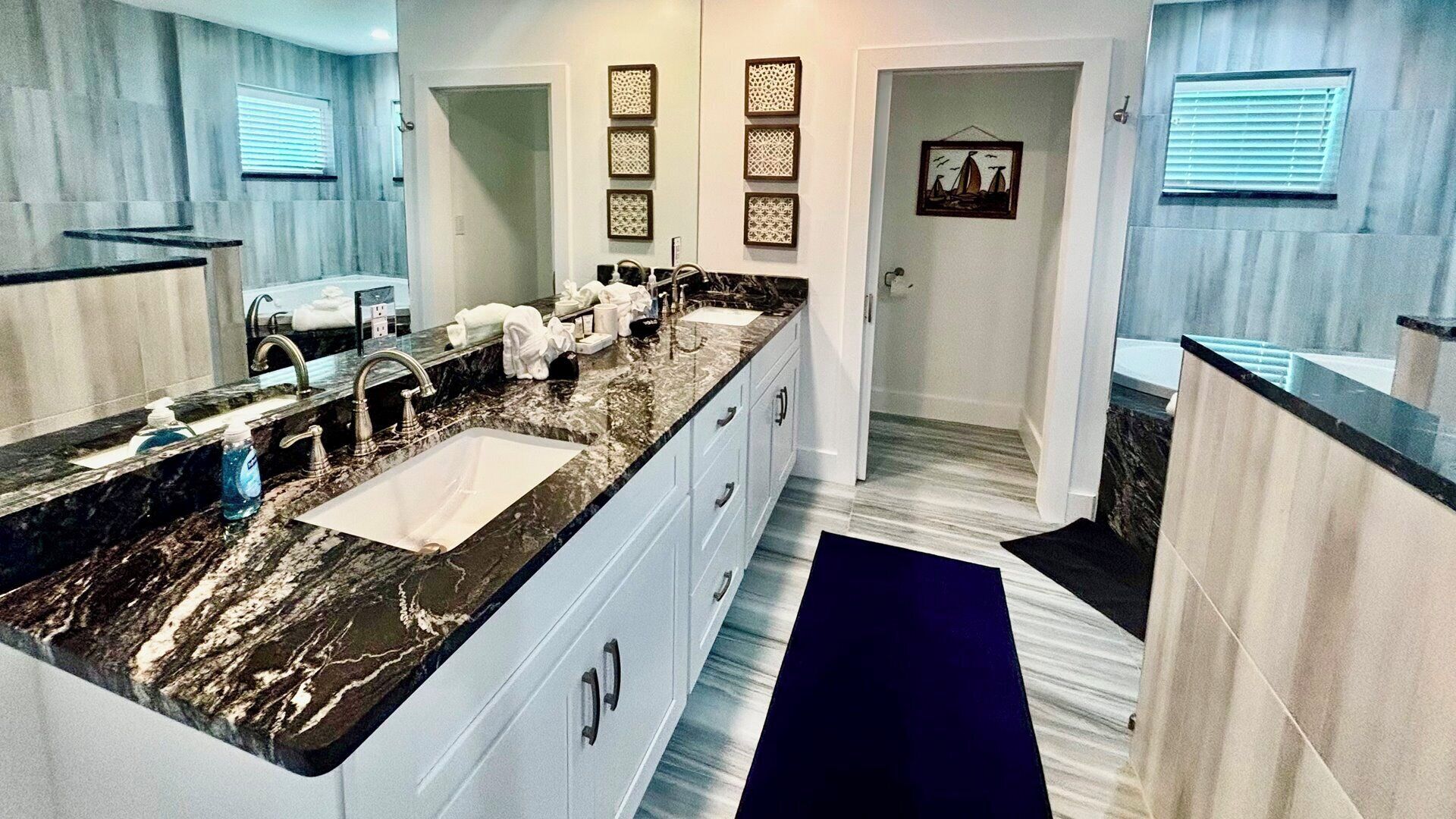 A modern bathroom with a large marble sink, white cabinetry, and a blue accent rug.