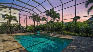 Une piscine dotée d’une structure en verre, entourée de palmiers et offrant une vue imprenable sur le coucher de soleil.