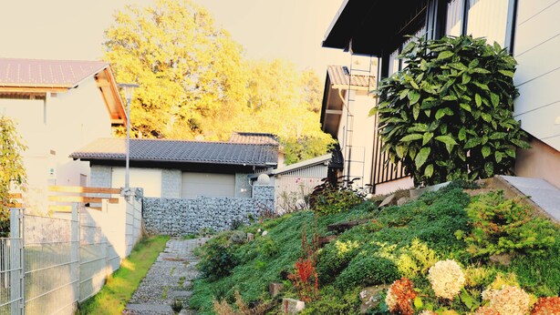 A pathway leading to a building with a traditional architectural style, surrounded by lush greenery and flowering plants. - Stylish and artistic apartment with 400 sqm garden & massage and Ayurveda (Grainet)