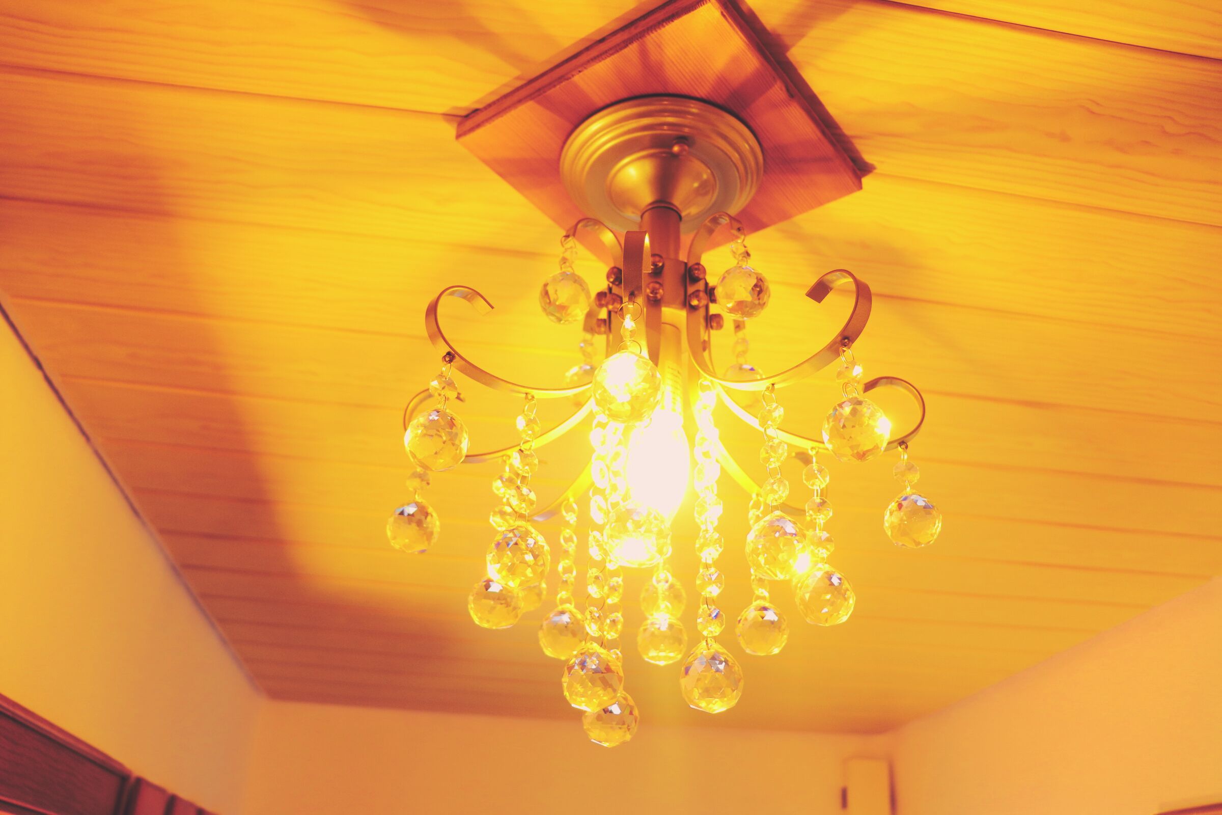 A chandelier with multiple light bulbs and crystal decorations hanging from a wooden ceiling.