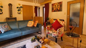 A living room with a blue sofa, a floral armchair, a small table with a lamp, and a wall-mounted heater. - Stylish and artistic apartment with 400 sqm garden & massage and Ayurveda (Grainet)