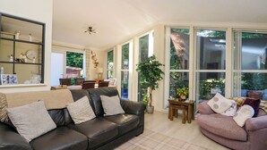 Ein geräumiges Wohnzimmer mit einem schwarzen Ledersofa, einem rosa Sessel und einem Essbereich mit Tisch und Stühlen.