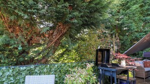 Eine Terrasse mit Korbmöbeln, einem blauen Blumentopf, einem Grill und einer Pergola.