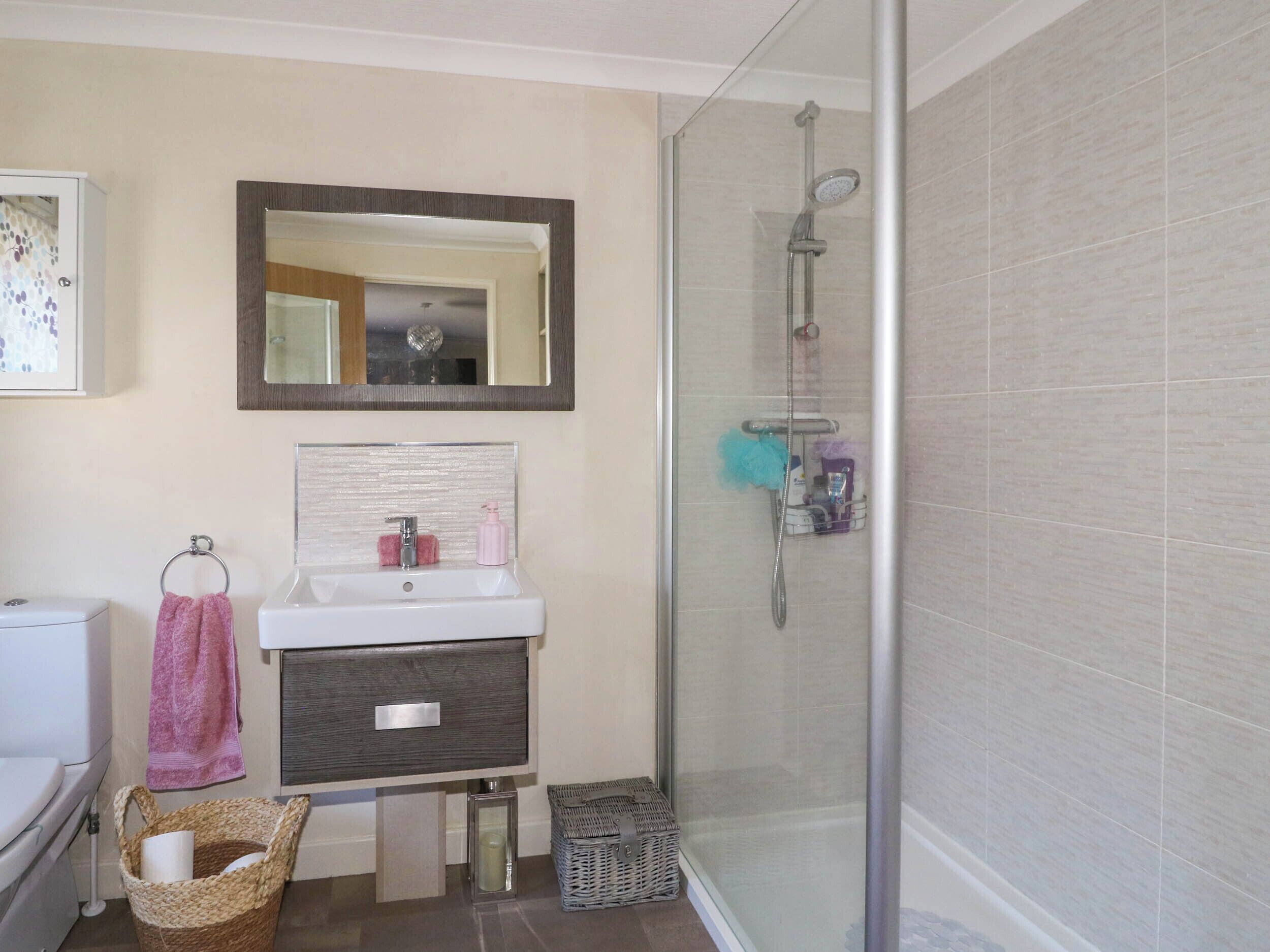 A bathroom with a glass shower enclosure, a white sink, a mirror, and a towel rack.