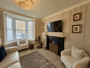 Una sala de estar con chimenea, un televisor montado encima y dos sofás.