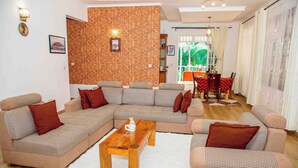 A living room with a sectional sofa, a wooden coffee table, and a brick accent wall. - Kindo Kicha Farmhouse (Moshi)