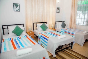 A hotel room with three single beds, each with a striped bedspread, a pillow, and a bedside table with a lamp. - Kindo Kicha Farmhouse (Moshi)